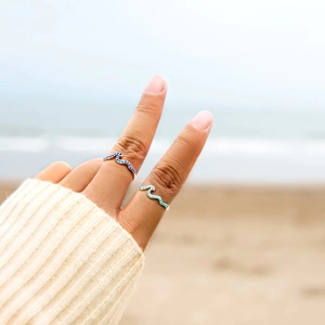 S925 sterling silver wave rings with blue zircons worn against a beach background