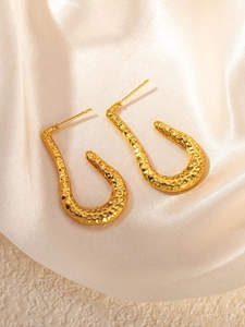 Macro detail of hammered gold U-shape earrings on elegant silk and stone textures