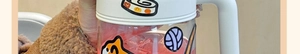 Close-up of glass tea mug with cartoon pattern, white lid and ergonomic handle