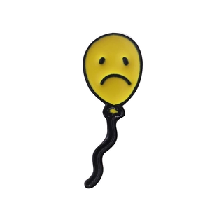 Détail macro d'un pin's en émail jaune représentant un ballon au visage triste et pleurant