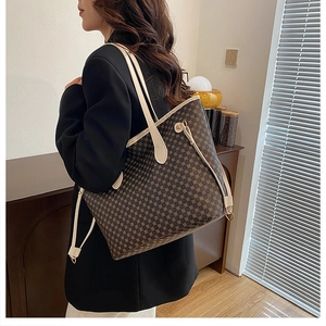 Brown checkered tote bag worn over the shoulder by a model in a cozy interior setting