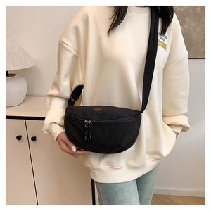 Detalle de un bolso bandolera de nailon negro con correa ajustable llevado por modelo