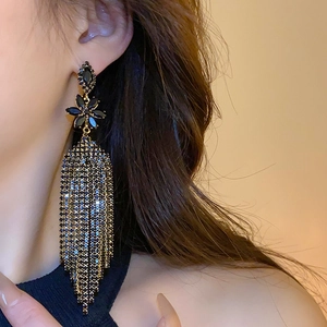 Dettaglio orecchini a fiore nero con lunghe nappe metalliche indossati da una modella
