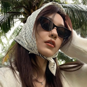 Close-up of black cat-eye sunglasses with a branded silk headscarf in vacation style
