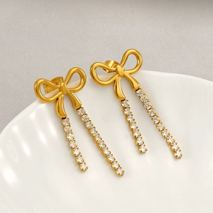 Elegant gold bow earrings with crystal tassels on a white ceramic plate backdrop