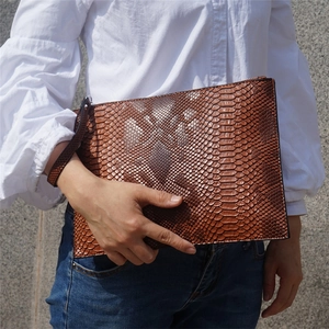 Brown snakeskin clutch bag with wristlet strap held by a model in casual white shirt