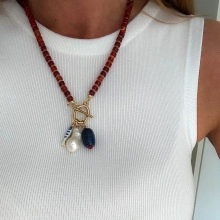 Detail of red beaded necklace with irregular pearl and blue fish pendant on a model
