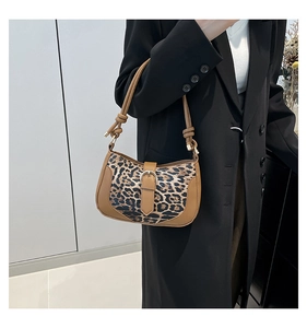 Close-up of leopard print shoulder bag with brown trim and metal buckle on black coat