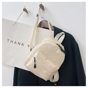 Classic beige nylon backpack for women hanging with a black blazer on a minimalist background
