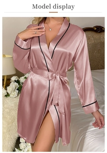 Detail of pink satin bathrobe with black trim and waist tie in a cozy bedroom setting