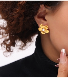 Détail de boucle d'oreille fleurie dorée avec perle blanche sur mannequin en col roulé