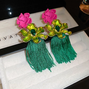 Détail de boucles d'oreilles bohèmes avec de longs pompons verts et des fleurs roses