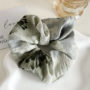 Détail d'un chouchou à motif floral vert sauge en tissu crêpé texturé sur plateau
