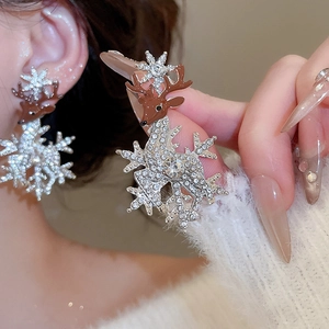 Close-up of crystal reindeer and snowflake stud earrings with soft brown pompom detail