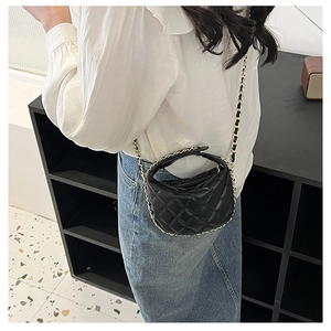 Detail of a black quilted mini crossbody bag with gold chain strap on a model