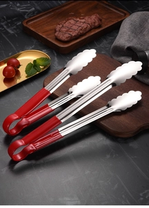Three stainless steel food tongs with red handles on a dark kitchen tabletop with steak