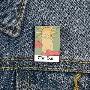 Detail of The Sun Tarot Cat enamel pin styled on a blue denim jacket pocket