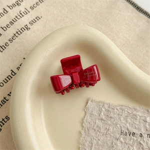 Detail of red acetate bow hair claw with gold lettering on a minimalist tray