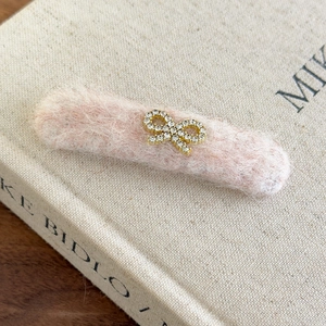 Detail of pink plush hair clip featuring a gold rhinestone bow on an open book