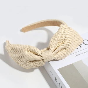 Detailed view of a beige woven straw headband featuring a large stylish bow decoration