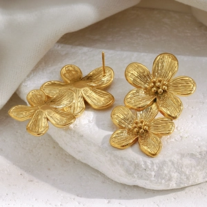 Detailed macro shot of vintage double-layered gold floral earrings on white stone