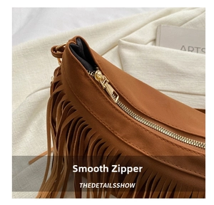 Detailed macro view of the smooth golden metal zipper on this brown suede tassel handbag