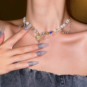 Detail of layered pearl necklace with square crystals and golden heart pendant