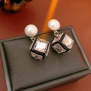 Close-up of pearl studs with black cubic crystal pendants on a luxury leather jewelry box