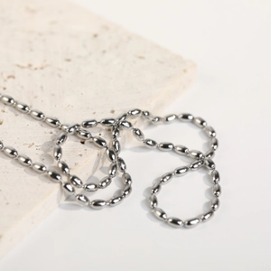Minimalist silver stainless steel rice bead necklace on a beige stone background