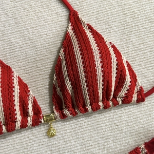 Détail d'un haut de bikini en crochet à rayures rouge et beige avec pendentif coquillage