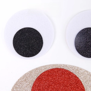 Close-up of DIY felt Christmas stickers with sparkling glitter surface and large round eyes