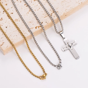 Gold and silver stainless steel plaid cross necklaces on a beige travertine stone