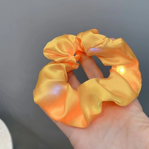 Detailed view of an orange satin LED scrunchie showing glowing light beads on silk fabric