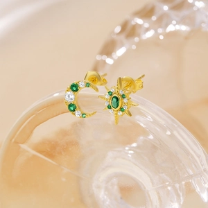 Detailed macro view of asymmetric gold star and moon stud earrings with green crystals