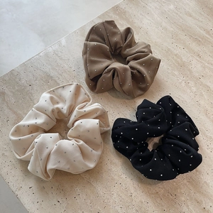 Three elegant rhinestone-studded scrunchies in cream, khaki, and black on marble stone