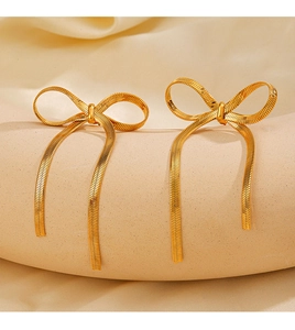 Mise à plat de boucles d'oreilles nœud en acier doré 18 carats sur tissu de soie beige