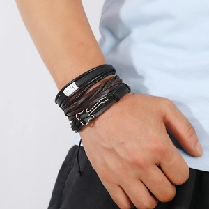Detail of multi-layer leather bracelet with woven cords and silver guitar pendant charm