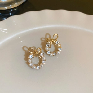 Close-up of golden bow earrings with pearls and rhinestones on a ceramic plate