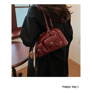 Detail of burgundy patent leather shoulder bag with front buckle pockets and bear charm