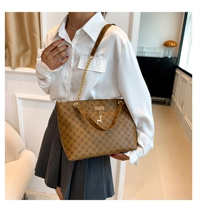Close-up of brown tote bag with gold deer charm and chain strap shown on model