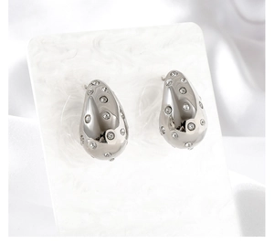 Macro shot of silver teardrop earrings with pavé zircons on marble and silk background