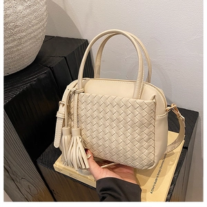 Detailed view of cream woven leather handbag with tassels on a rustic wood base
