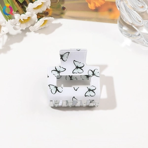 Detail view of a white acrylic hair claw clip with blue and black butterfly prints