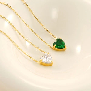 Golden heart pendant necklace with emerald green and clear zircon on a white bowl