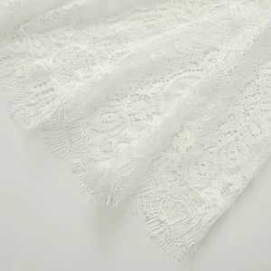 Dettaglio in primo piano del tessuto in pizzo bianco con motivi intricati e bordi a ciglia