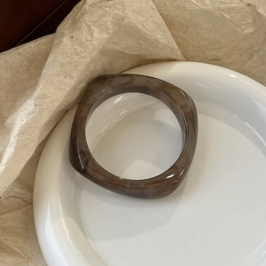 Detailed macro view of a brown tortoiseshell resin bangle on a white ceramic plate