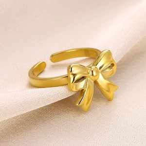 Macro detail of a golden bow ring with adjustable open band on beige silk fabric