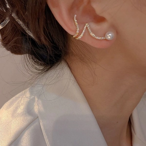 Detailed close-up of wavy gold ear cuff featuring sparkling cubic zirconia and a white pearl