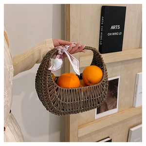 Close-up of a woven basket bag with a silk ribbon detail and fresh oranges inside