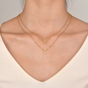 Detailed view of layered gold-tone titanium necklaces featuring capital R and Z letter charms